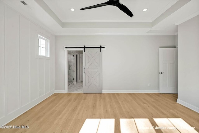 unfurnished bedroom featuring light wood-style floors, baseboards, a tray ceiling, and a barn door