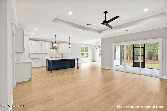 kitchen with a raised ceiling, open floor plan, light countertops, light wood-style floors, and ceiling fan with notable chandelier