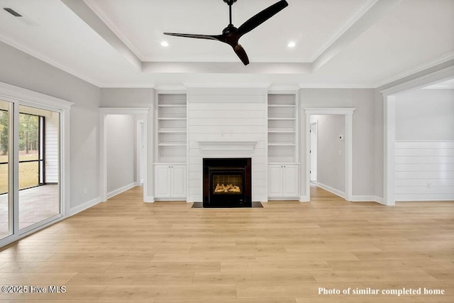 unfurnished living room with light wood-style floors, a fireplace, a tray ceiling, and ornamental molding