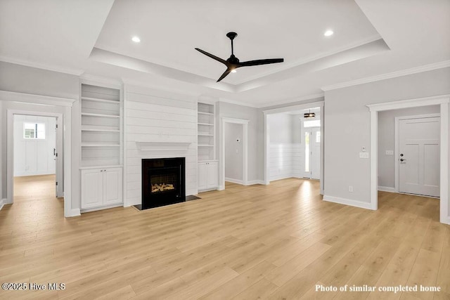 unfurnished living room with light wood-style floors, a raised ceiling, a large fireplace, and ceiling fan