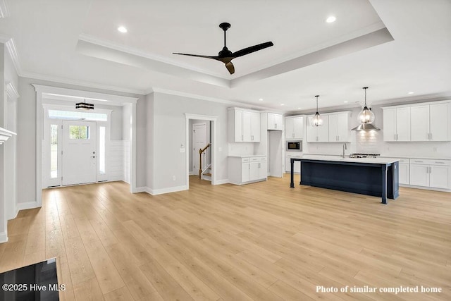 unfurnished living room featuring ornamental molding, a tray ceiling, stairway, and light wood-style flooring