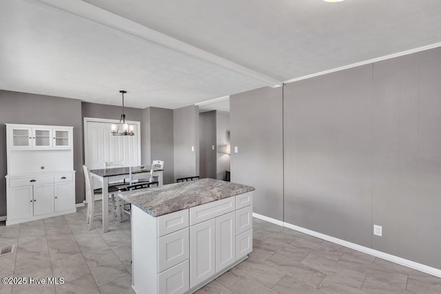 kitchen with white cabinetry, hanging light fixtures, a center island, a notable chandelier, and light stone countertops