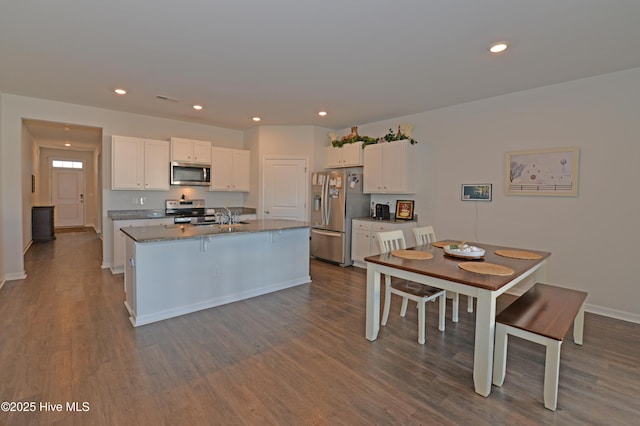 kitchen with white cabinetry, dark stone countertops, an island with sink, stainless steel appliances, and hardwood / wood-style floors