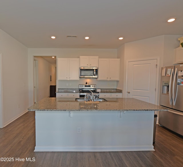 kitchen with stainless steel appliances, white cabinetry, an island with sink, and light stone counters