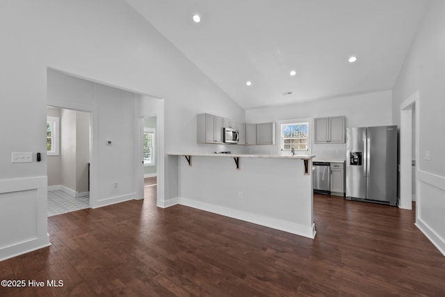 kitchen with a breakfast bar area, gray cabinetry, high vaulted ceiling, stainless steel appliances, and a wealth of natural light