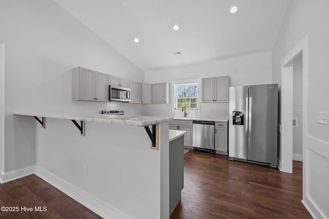 kitchen featuring gray cabinetry, dark hardwood / wood-style flooring, a kitchen breakfast bar, kitchen peninsula, and stainless steel appliances