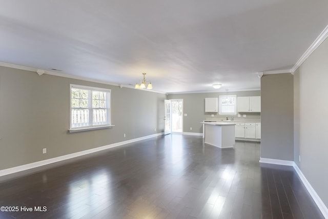 unfurnished living room with sink, a notable chandelier, dark wood-type flooring, and ornamental molding