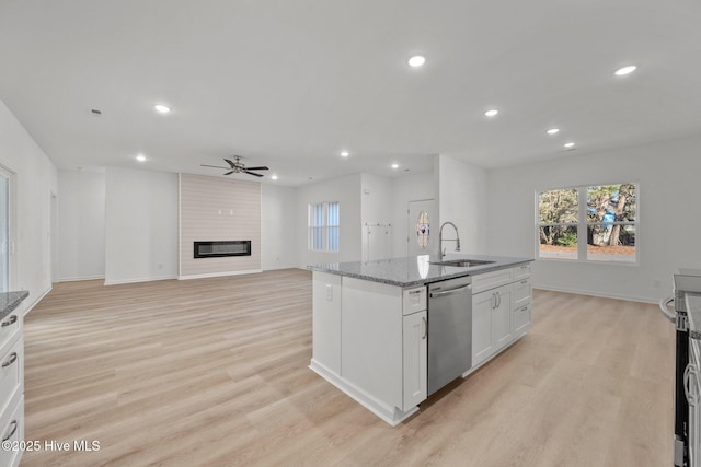 kitchen with sink, a large fireplace, dishwasher, an island with sink, and white cabinets