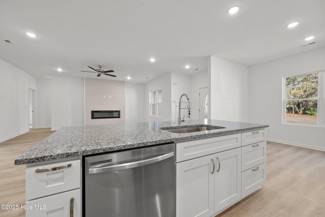 kitchen featuring stone counters, white cabinetry, dishwasher, sink, and a large fireplace