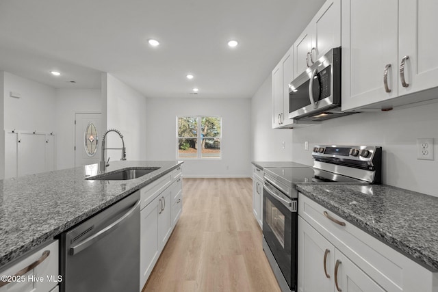 kitchen featuring sink, white cabinetry, stainless steel appliances, dark stone counters, and light wood-type flooring