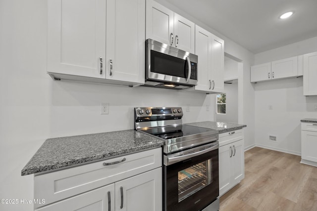 kitchen with white cabinetry, appliances with stainless steel finishes, and dark stone counters