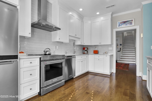 kitchen featuring crown molding, white cabinets, appliances with stainless steel finishes, and wall chimney range hood