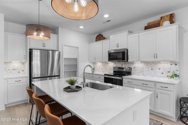 kitchen with white cabinetry, stainless steel appliances, sink, and a center island with sink