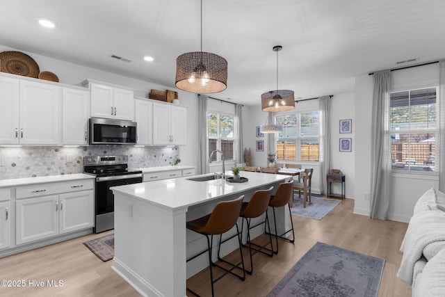 kitchen with appliances with stainless steel finishes, sink, white cabinets, and decorative light fixtures