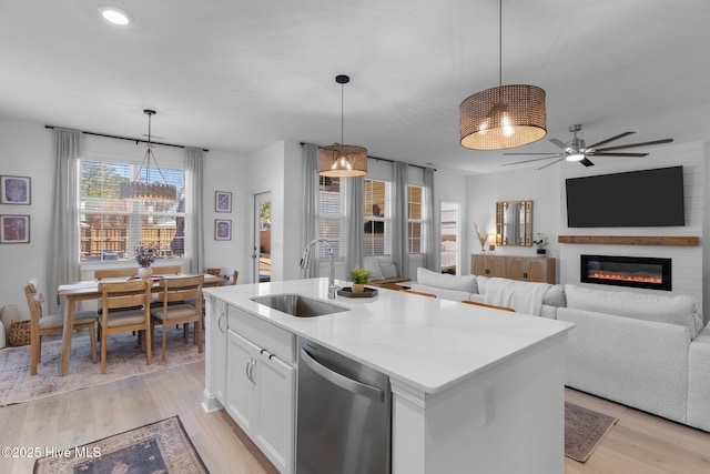 kitchen with pendant lighting, sink, white cabinets, stainless steel dishwasher, and a center island with sink