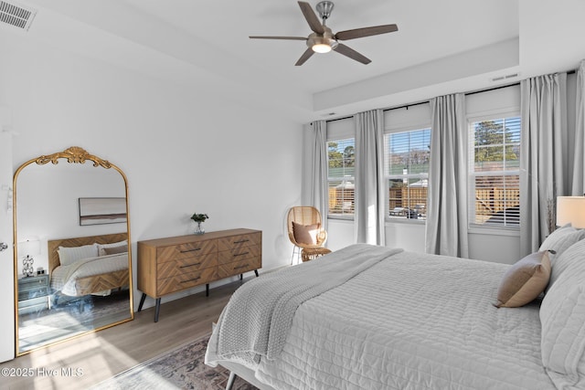 bedroom with hardwood / wood-style flooring, a raised ceiling, and ceiling fan