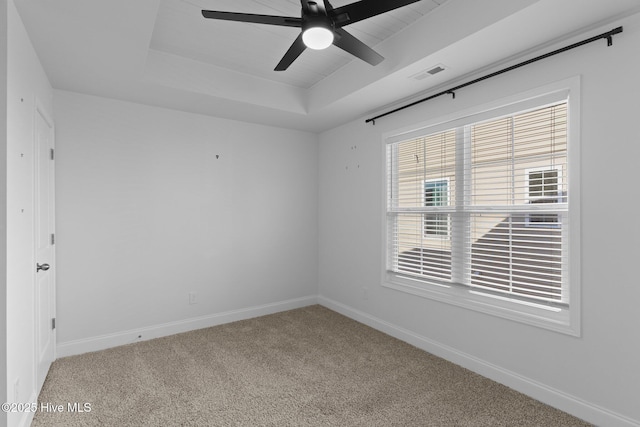 empty room with ceiling fan, light colored carpet, and a raised ceiling