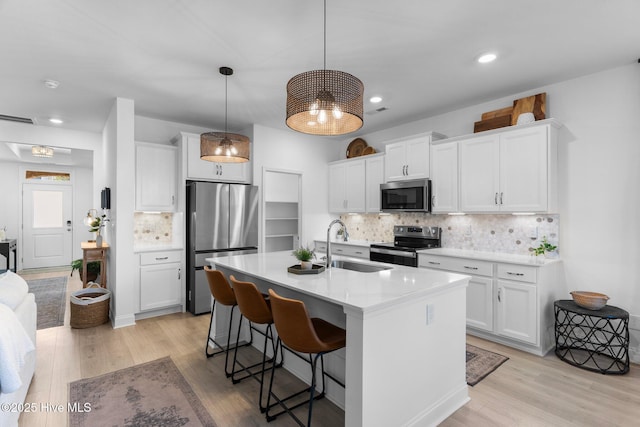 kitchen featuring sink, white cabinetry, hanging light fixtures, stainless steel appliances, and a kitchen island with sink