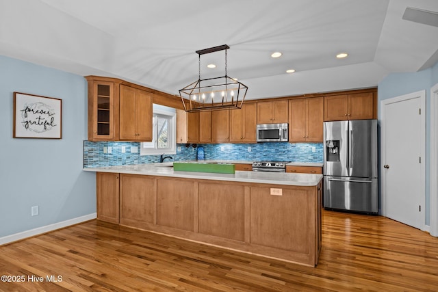 kitchen featuring pendant lighting, tasteful backsplash, kitchen peninsula, stainless steel appliances, and light wood-type flooring