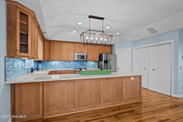 kitchen with pendant lighting, light hardwood / wood-style flooring, appliances with stainless steel finishes, backsplash, and kitchen peninsula