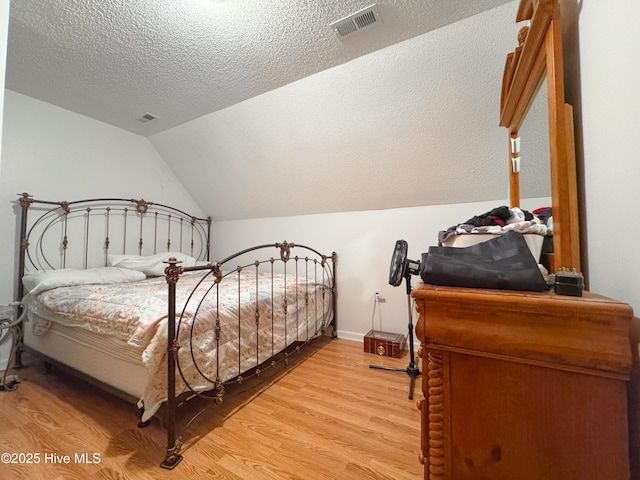 bedroom with vaulted ceiling, light hardwood / wood-style floors, and a textured ceiling