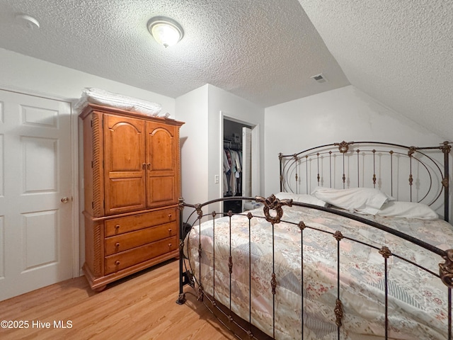 bedroom with a closet, lofted ceiling, a walk in closet, a textured ceiling, and light hardwood / wood-style flooring