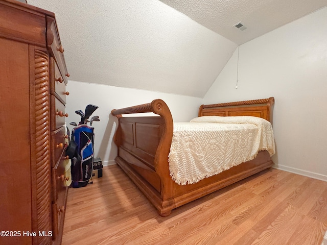 bedroom with lofted ceiling, light hardwood / wood-style floors, and a textured ceiling