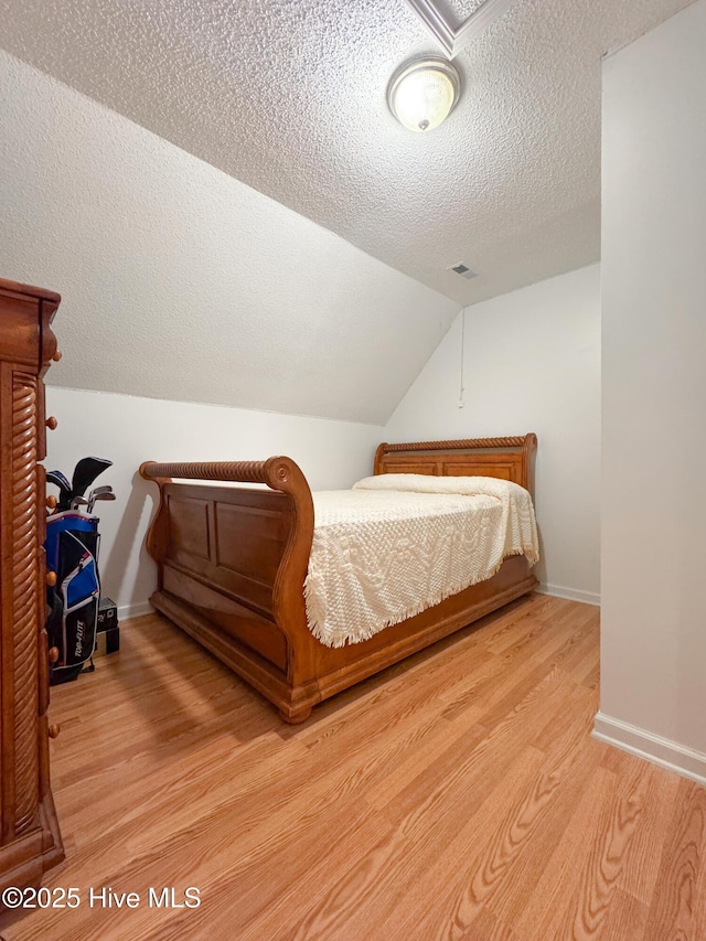 bedroom featuring lofted ceiling, hardwood / wood-style flooring, and a textured ceiling