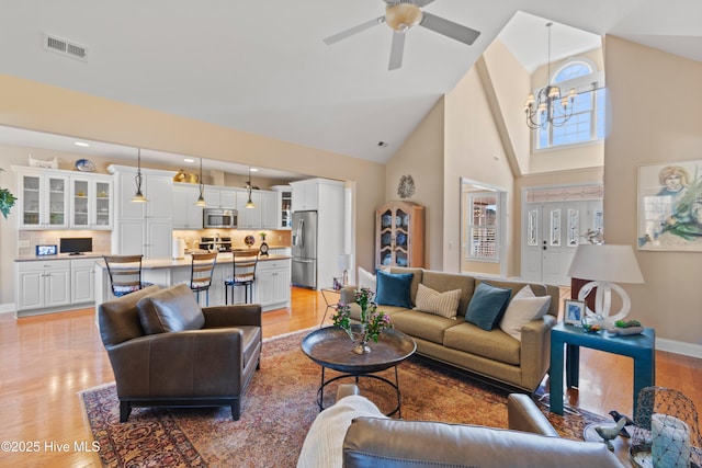 living room with ceiling fan with notable chandelier, high vaulted ceiling, and light wood-type flooring