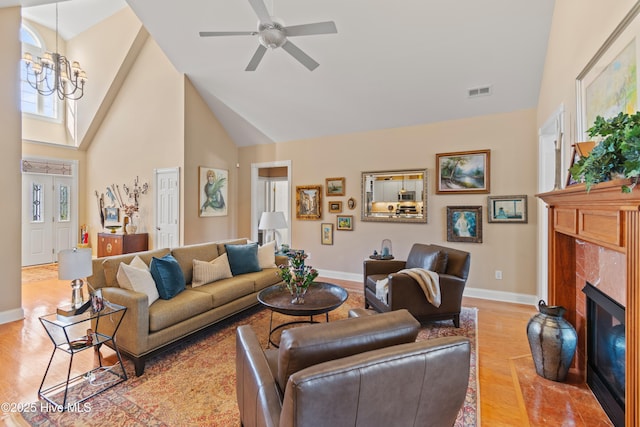 living room featuring high vaulted ceiling, ceiling fan with notable chandelier, a fireplace, and light hardwood / wood-style floors