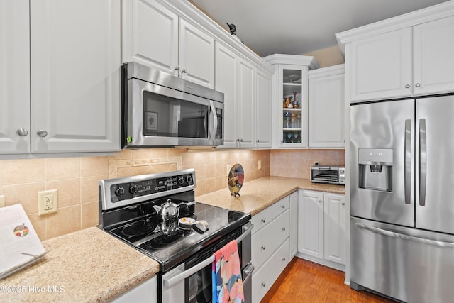 kitchen featuring white cabinetry, light stone counters, appliances with stainless steel finishes, light hardwood / wood-style floors, and decorative backsplash