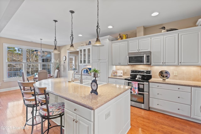 kitchen with pendant lighting, stainless steel appliances, light stone countertops, an island with sink, and white cabinets