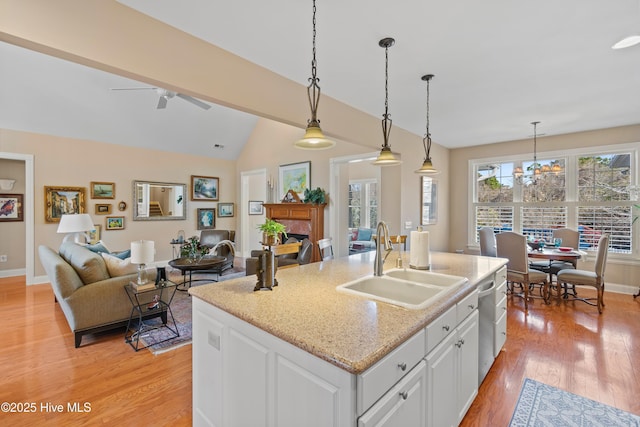 kitchen with sink, white cabinetry, hanging light fixtures, dishwasher, and an island with sink