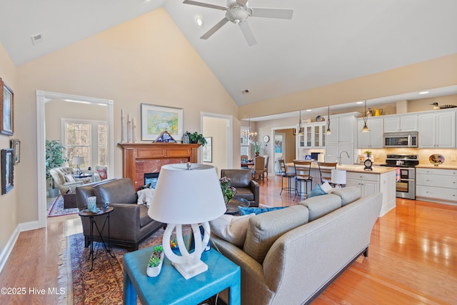 living room with sink, high vaulted ceiling, ceiling fan, and light wood-type flooring