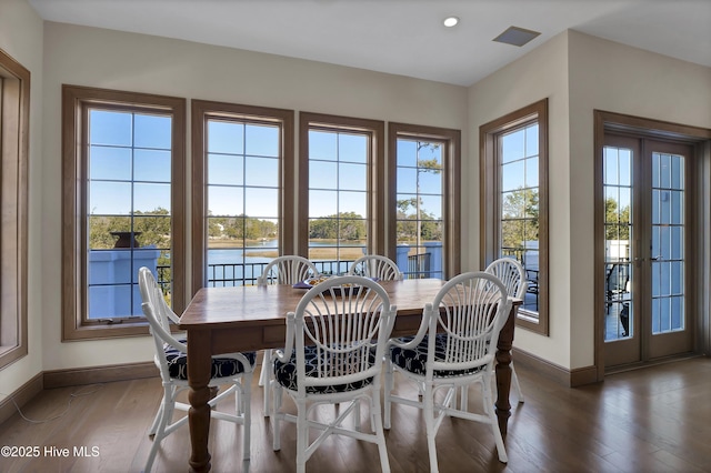 dining space featuring dark wood-type flooring, a water view, and french doors