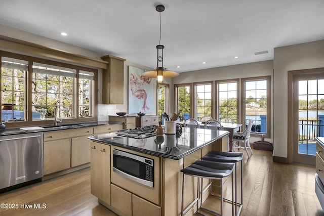 kitchen featuring a kitchen island, appliances with stainless steel finishes, decorative light fixtures, sink, and light hardwood / wood-style floors