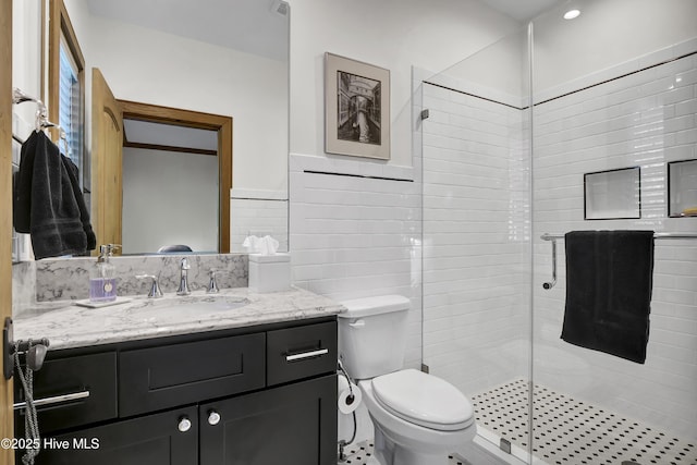 bathroom featuring vanity, toilet, a shower with shower door, and tile walls