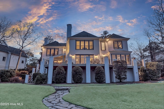 back house at dusk with a yard and a balcony