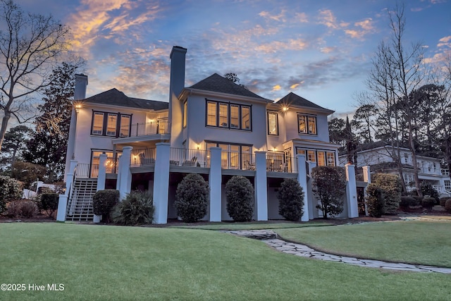 back house at dusk featuring a lawn and a balcony