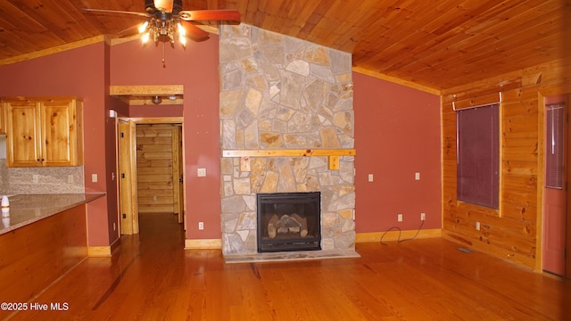 unfurnished living room with lofted ceiling, wood-type flooring, ornamental molding, a stone fireplace, and wooden ceiling