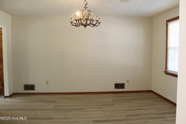 unfurnished room featuring hardwood / wood-style flooring, an inviting chandelier, and a textured ceiling