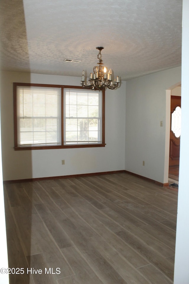 spare room with dark wood-type flooring, an inviting chandelier, and a textured ceiling