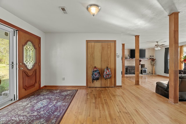 entrance foyer featuring decorative columns, a brick fireplace, a healthy amount of sunlight, and light hardwood / wood-style flooring