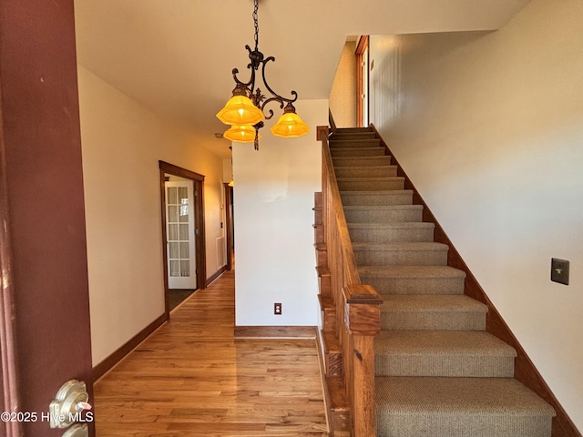 staircase with hardwood / wood-style floors and a chandelier