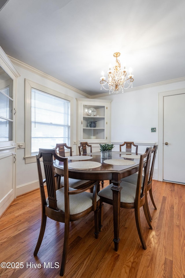 dining area with a notable chandelier, ornamental molding, and light wood-type flooring