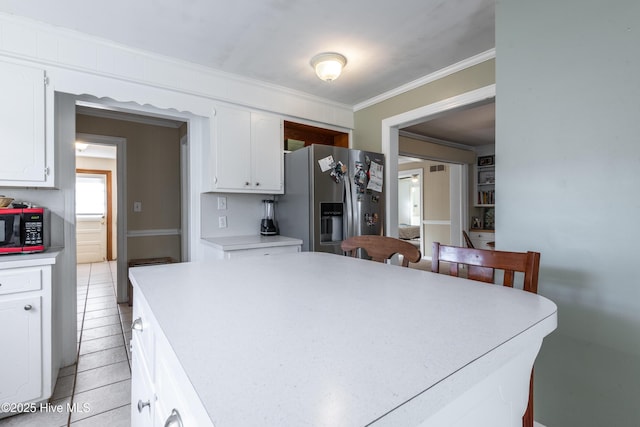 kitchen featuring light tile patterned flooring, ornamental molding, stainless steel fridge, and white cabinets