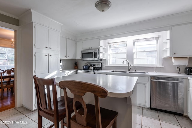 kitchen with sink, light tile patterned floors, appliances with stainless steel finishes, white cabinets, and a kitchen bar