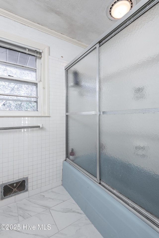 bathroom with tile walls and combined bath / shower with glass door