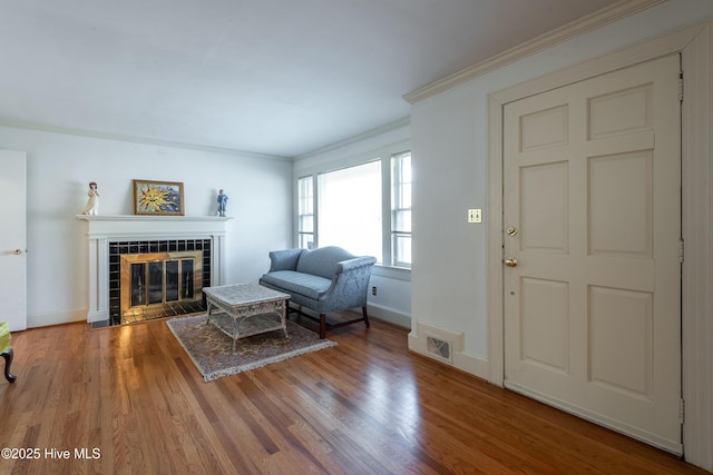 living room with wood-type flooring, ornamental molding, and a tile fireplace