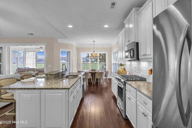 kitchen with sink, appliances with stainless steel finishes, a kitchen island with sink, dark stone countertops, and white cabinets